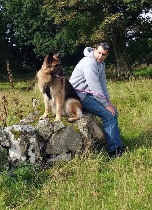 Sebastien Day sitting on a stone wall with Chai, a German Shepherd